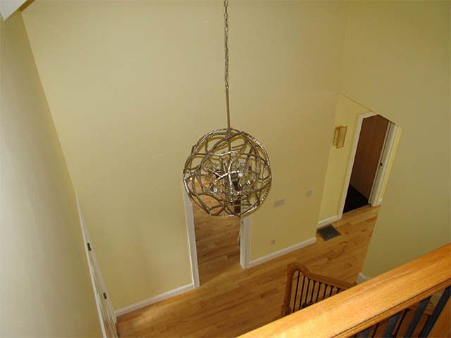 High-ceiling foyer with hanging spherical light fixture, wood floors, and open doorways.