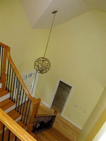 Staircase with wood railings, hanging spherical light, and a doorway in a beige foyer.