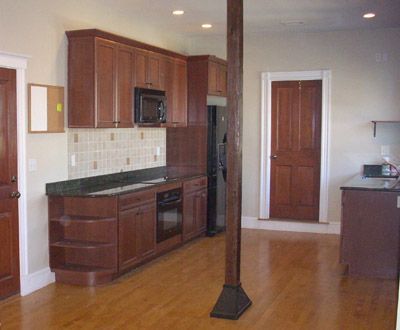 Empty kitchen with dark wood cabinets, black appliances, and a wood floor around a support column