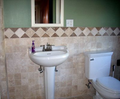 Small bathroom with a pedestal sink, toilet, and tiled walls in beige and green.