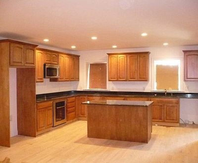 Spacious modern kitchen with wood cabinets, black countertops, and a central island under recessed lights