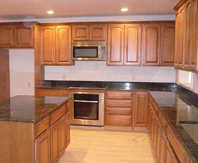 Spacious kitchen with wood cabinets, black countertops, stainless appliances, and light wood flooring.