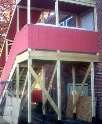 Partially built house with red siding and exposed wooden framing on support posts