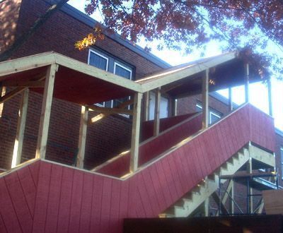 Red wooden staircase and porch on a house with white railings and brick walls under trees