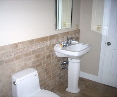 Bathroom with white toilet and pedestal sink, beige tiled wall, and frosted glass door