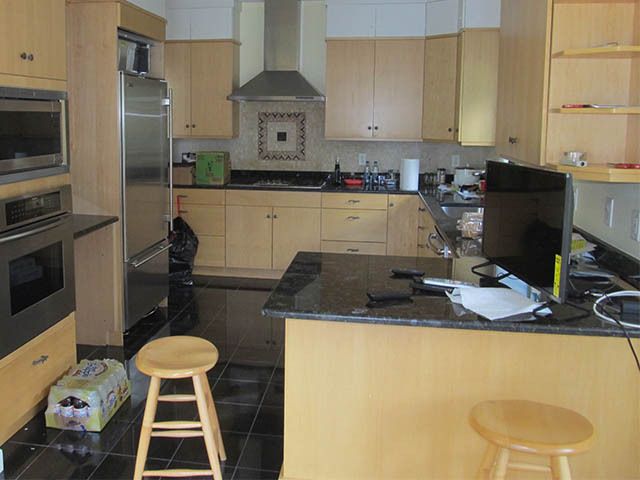 Modern kitchen with light wood cabinets, black countertops, stools, and a TV on the counter