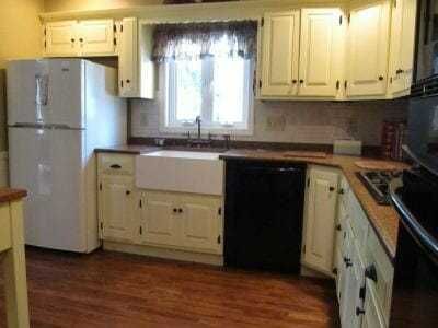 A bright kitchen with cream cabinets, white appliances, a farmhouse sink, and a wood floor.