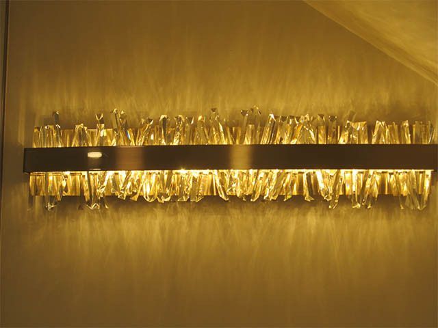 Warm-lit wall sconce with clear glass pendants on a textured gold wall