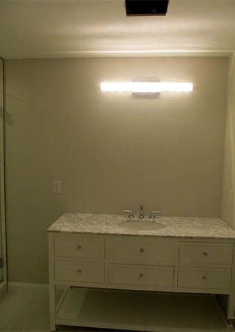 Small bathroom vanity with sink, drawers, and wall mirror light against beige walls.