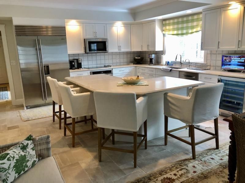 Modern white kitchen with a large island, cream barstools, and stainless steel appliances