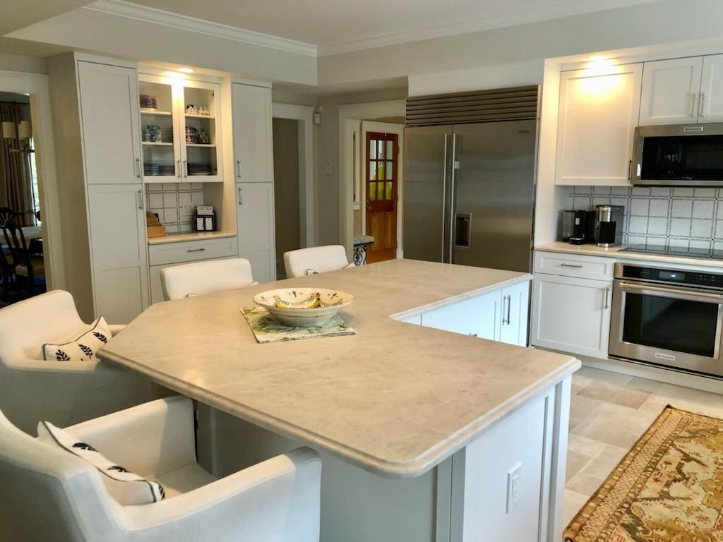 Bright white kitchen with a large beige island, built-in oven, and windowed cabinets