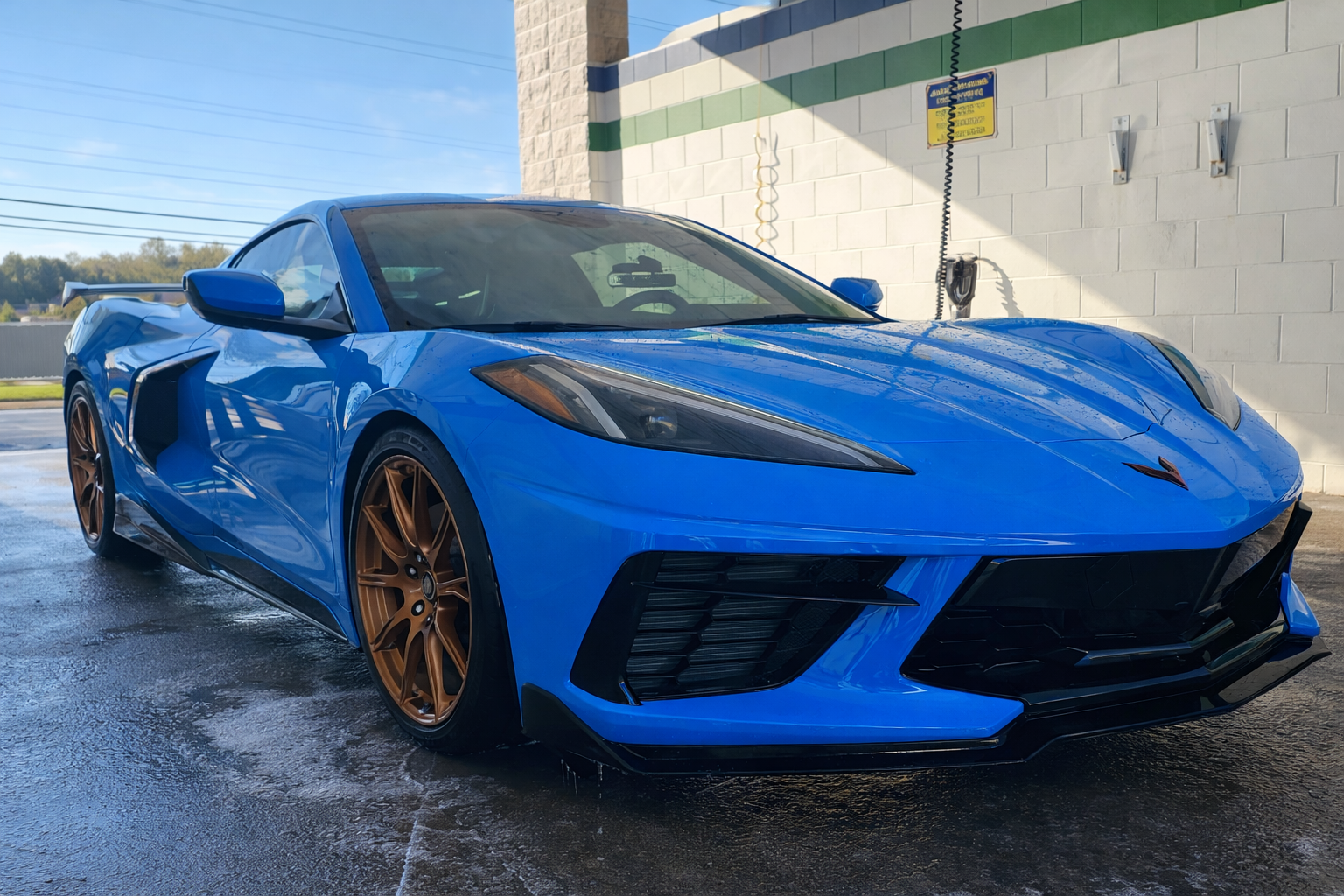 Bright blue Chevrolet Corvette with bronze wheels at a car wash.