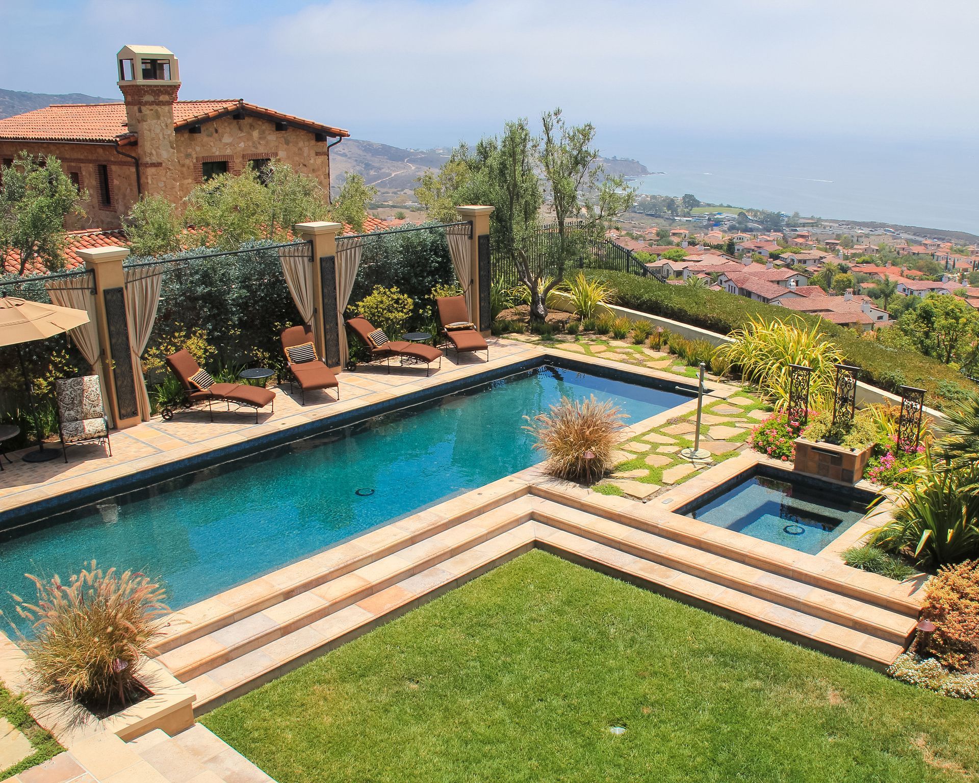 Modern hillside villa with turquoise pool, hot tub, and landscaped lawn overlooking a city view