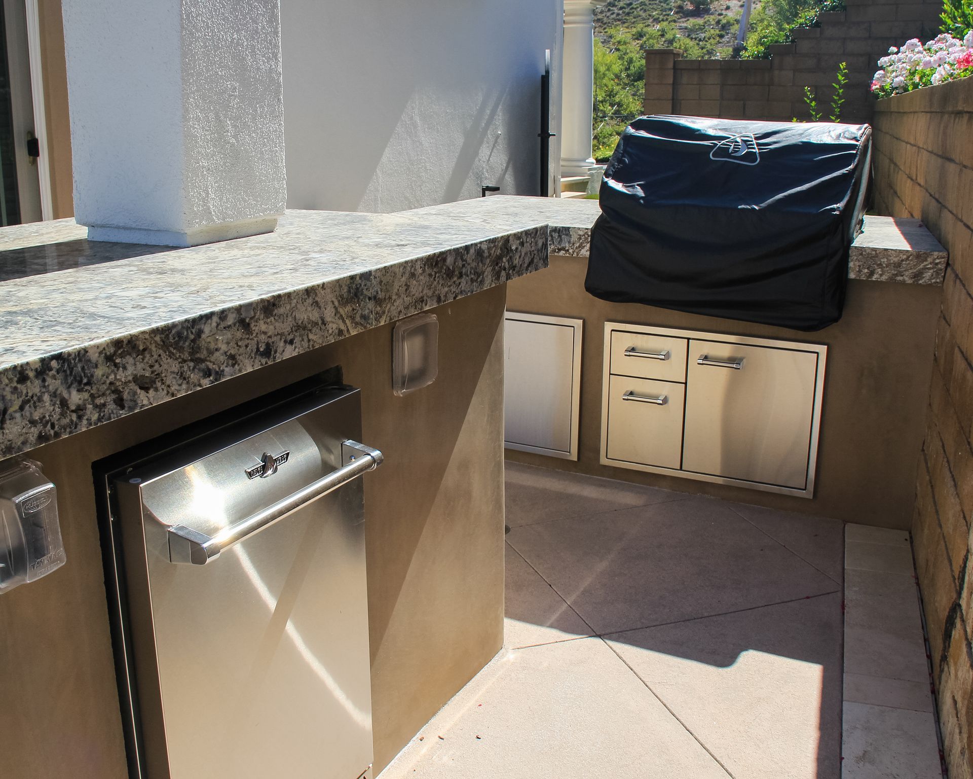 Outdoor patio with built-in grill, granite countertop, and storage cabinets, with a covered grill at right.