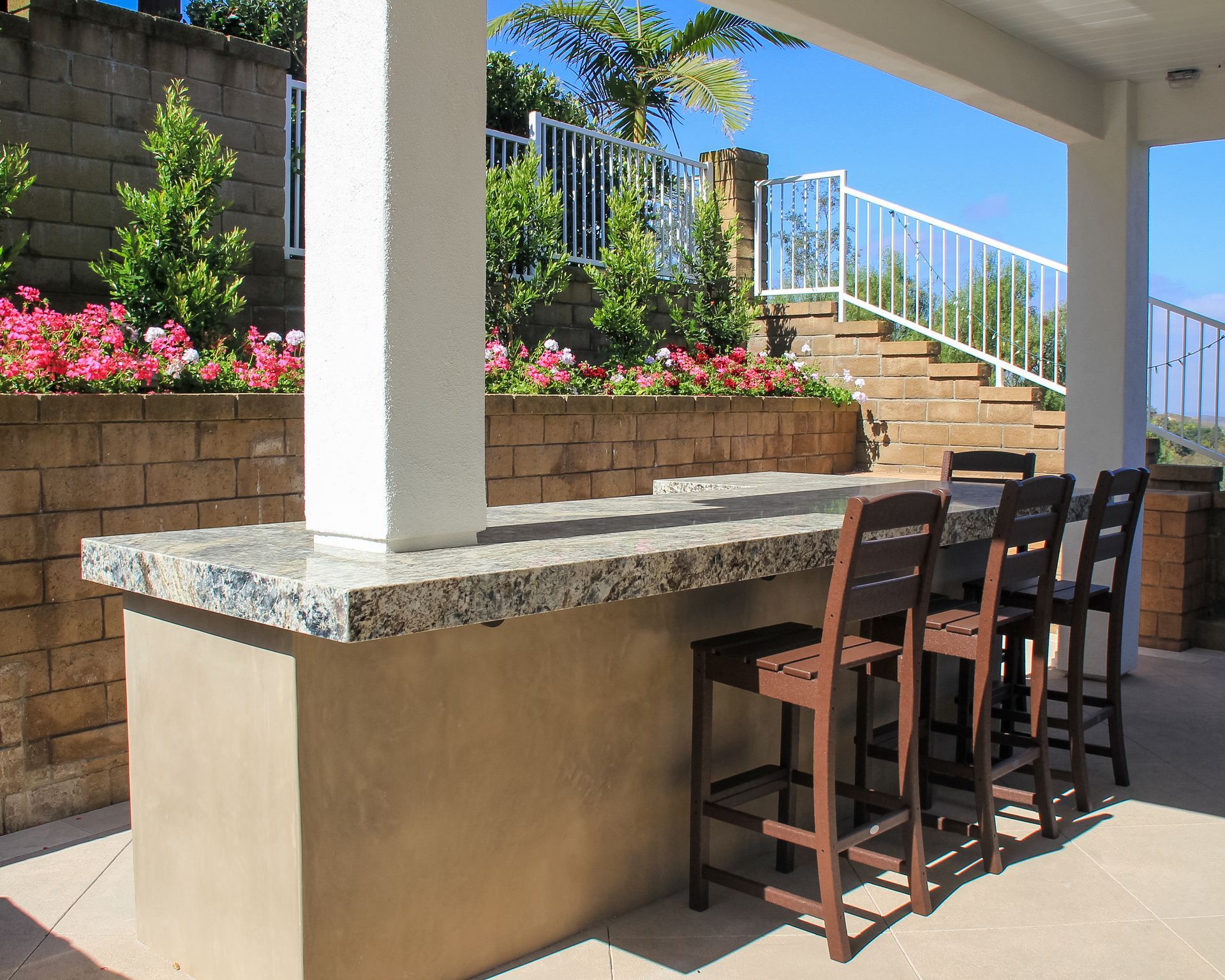 Outdoor patio with a stone counter, bar stools, and flower beds beside a staircase