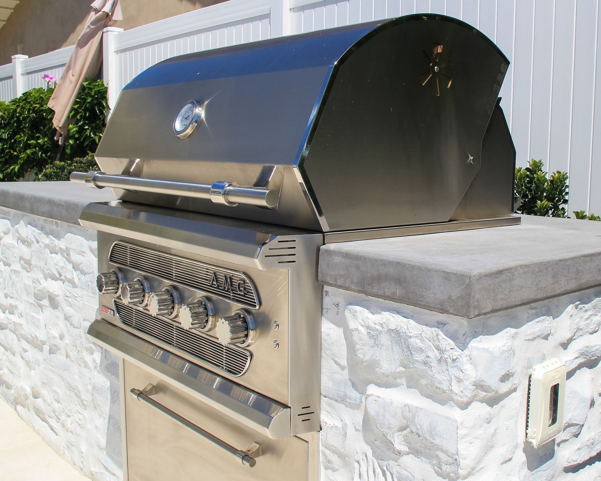 Built-in stainless steel outdoor grill with closed hood beside a stone patio wall