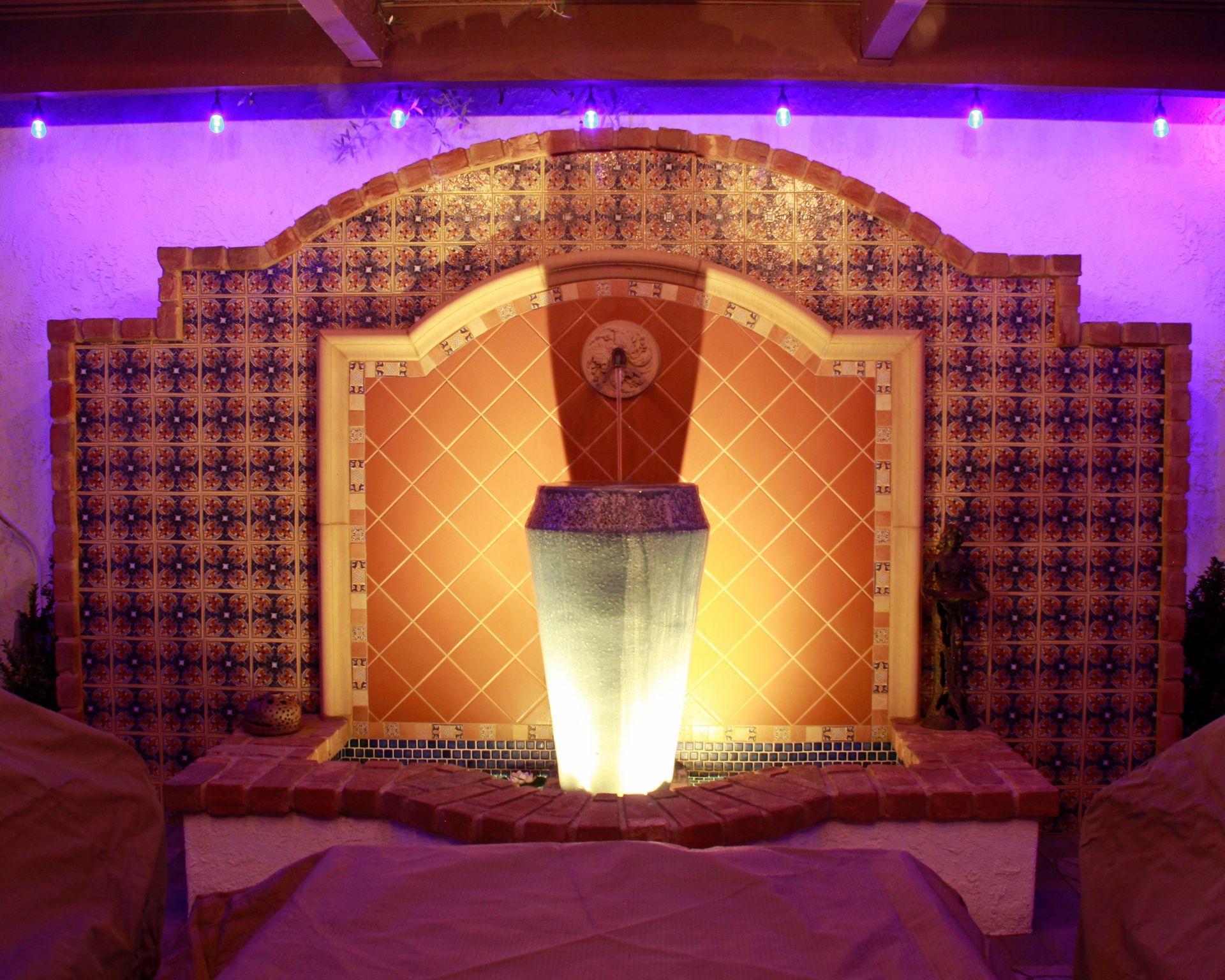 Decorative lit fountain with purple and orange mosaic backdrop in an indoor setting