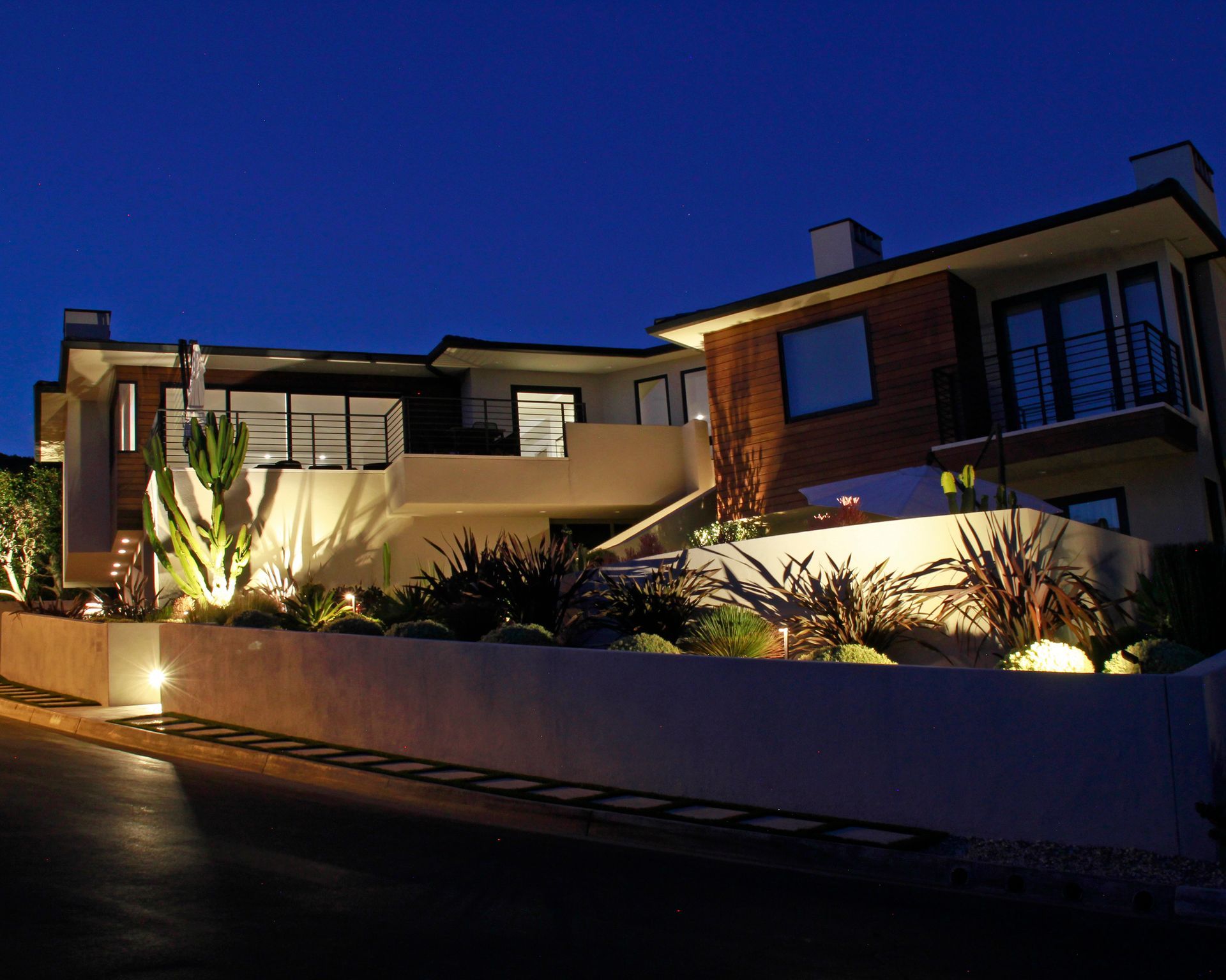 Modern house at dusk with landscaped front yard and warm exterior lighting