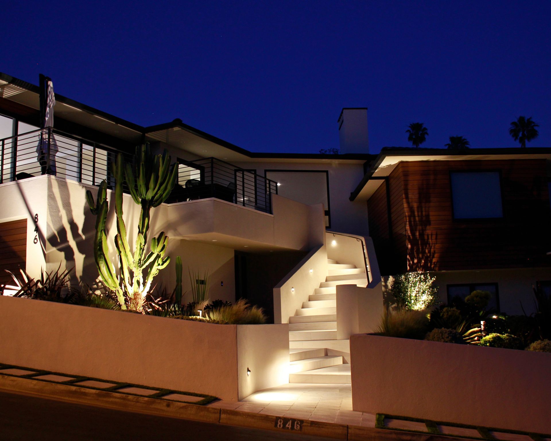 Nighttime view of a modern house with illuminated front steps and desert landscaping