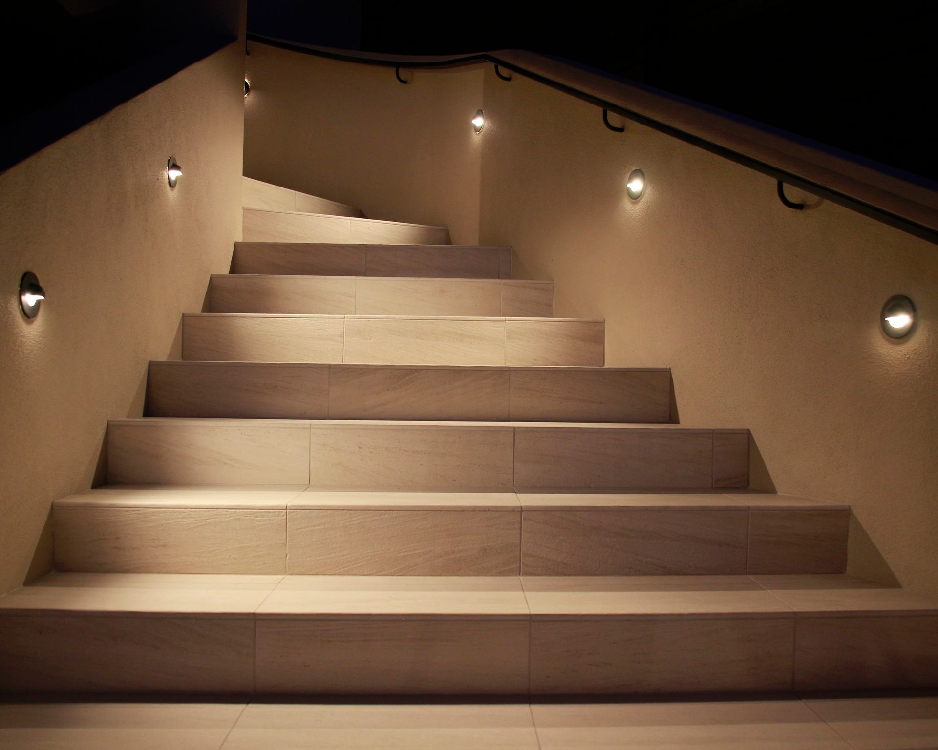 Dimly lit indoor staircase with beige steps and wall lights on both sides