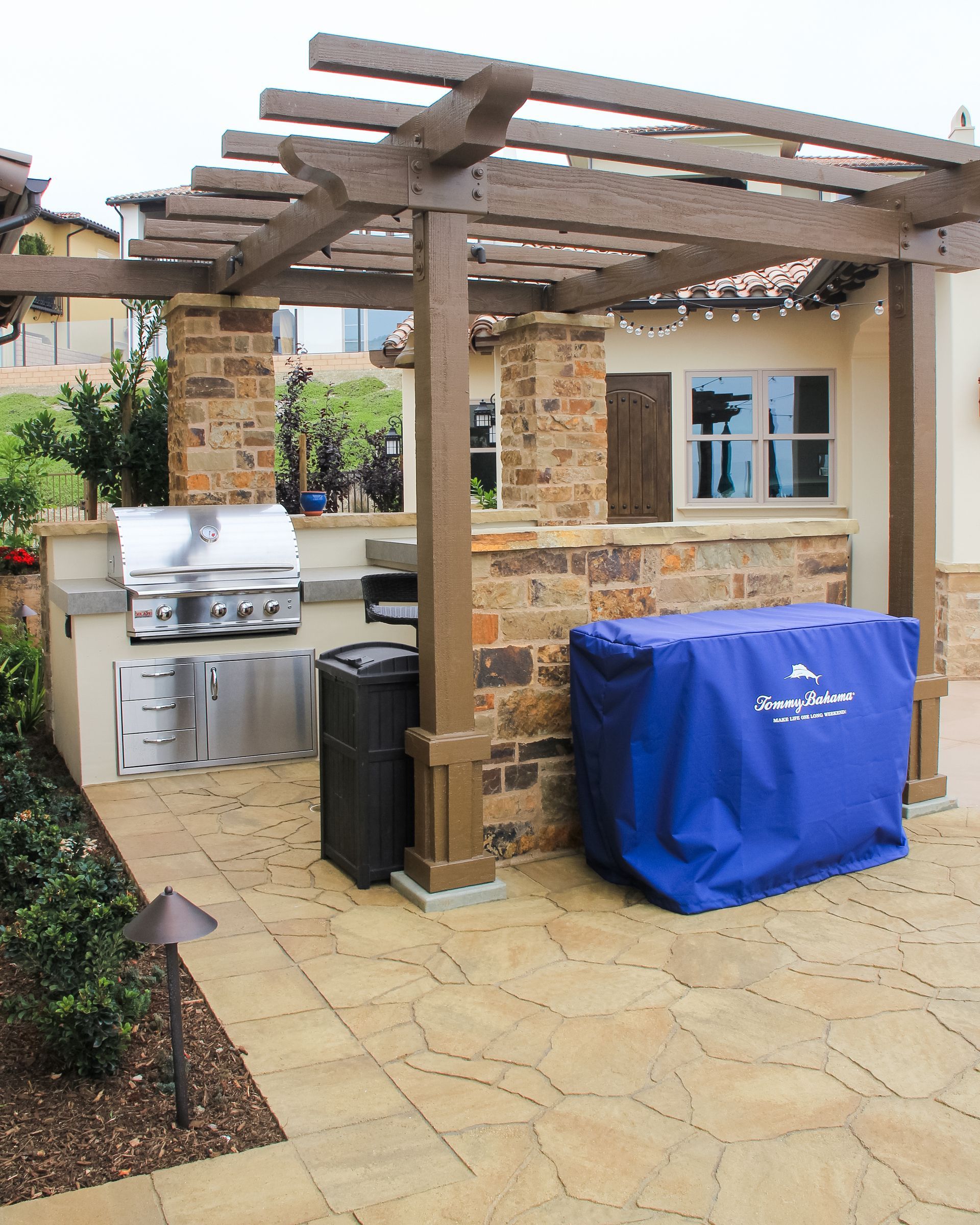 Backyard patio with a grill, stone pergola, and blue-covered outdoor furniture by a house