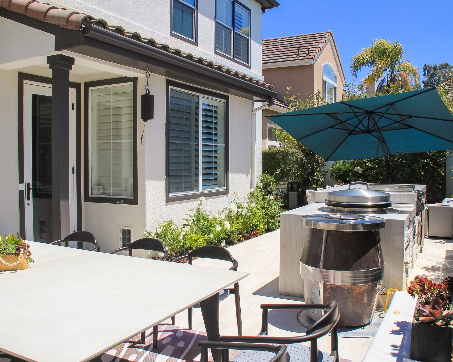 Backyard patio with outdoor table, grill, and blue umbrella beside a house