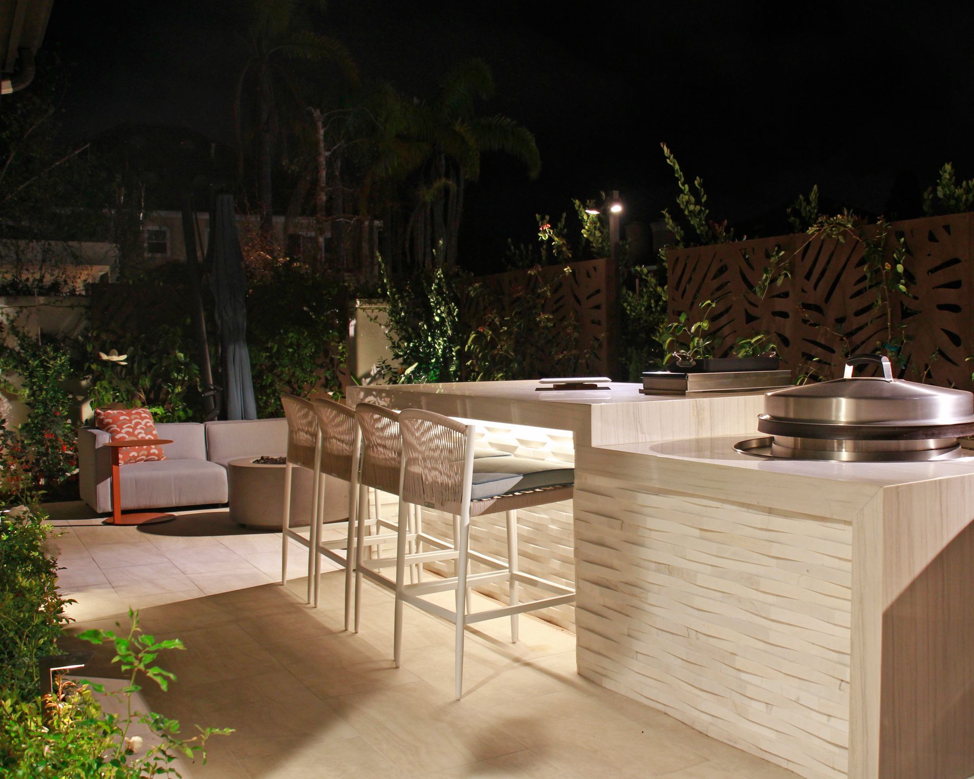 Outdoor patio with a built-in stone grill, bar seating, and lounge chairs at night