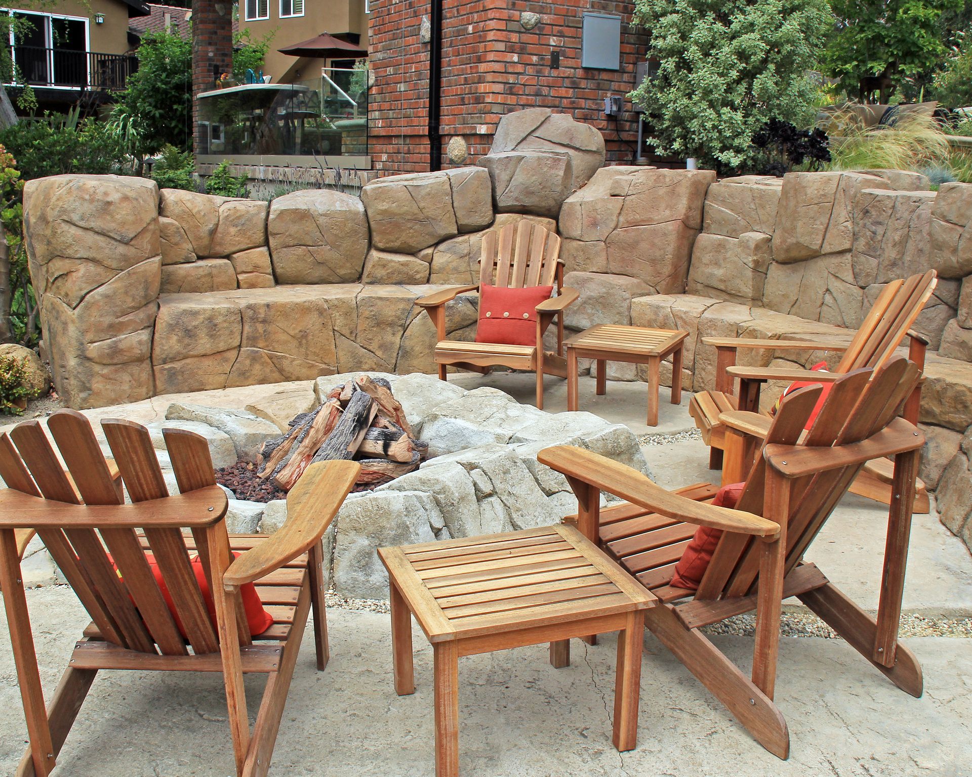 Stone fire pit with wooden Adirondack chairs arranged on a patio in a garden setting