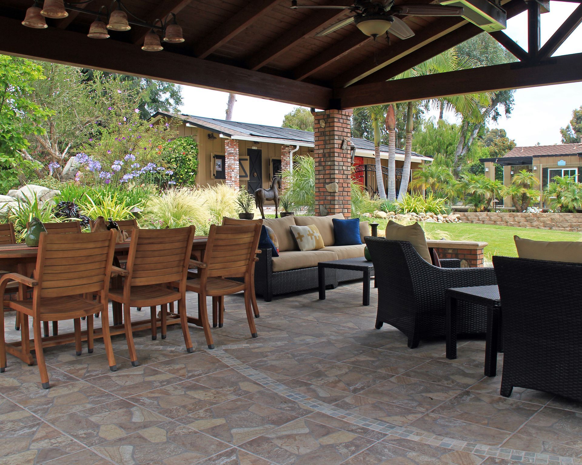 Covered patio with wooden and wicker seating, stone floor, and a landscaped garden view.