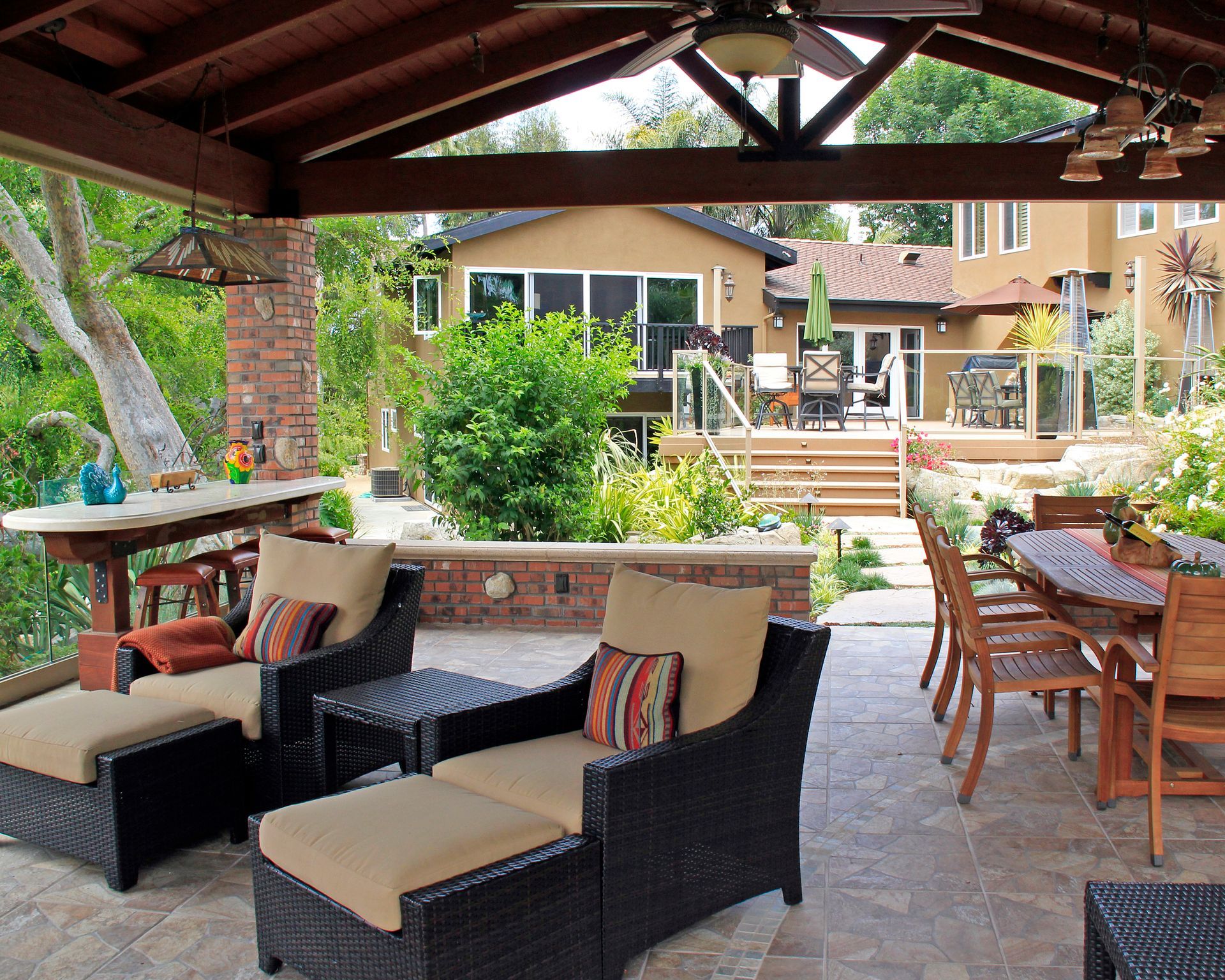 Covered outdoor patio with wicker seating, dining table, and garden view overlooking a pool and resort-style buildings