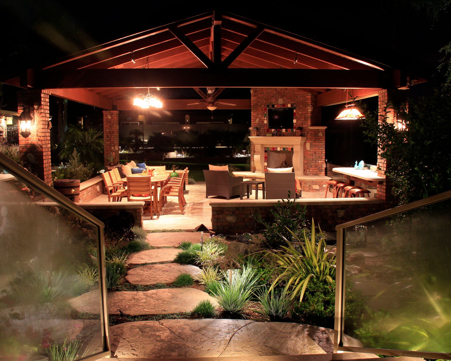 Warmly lit outdoor patio with stone steps, seating, and plants at night