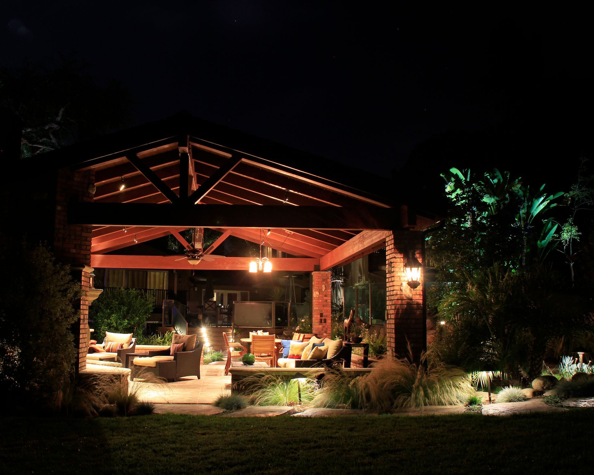 Cozy lit outdoor patio at night with wooden gazebo, chairs, and garden lighting