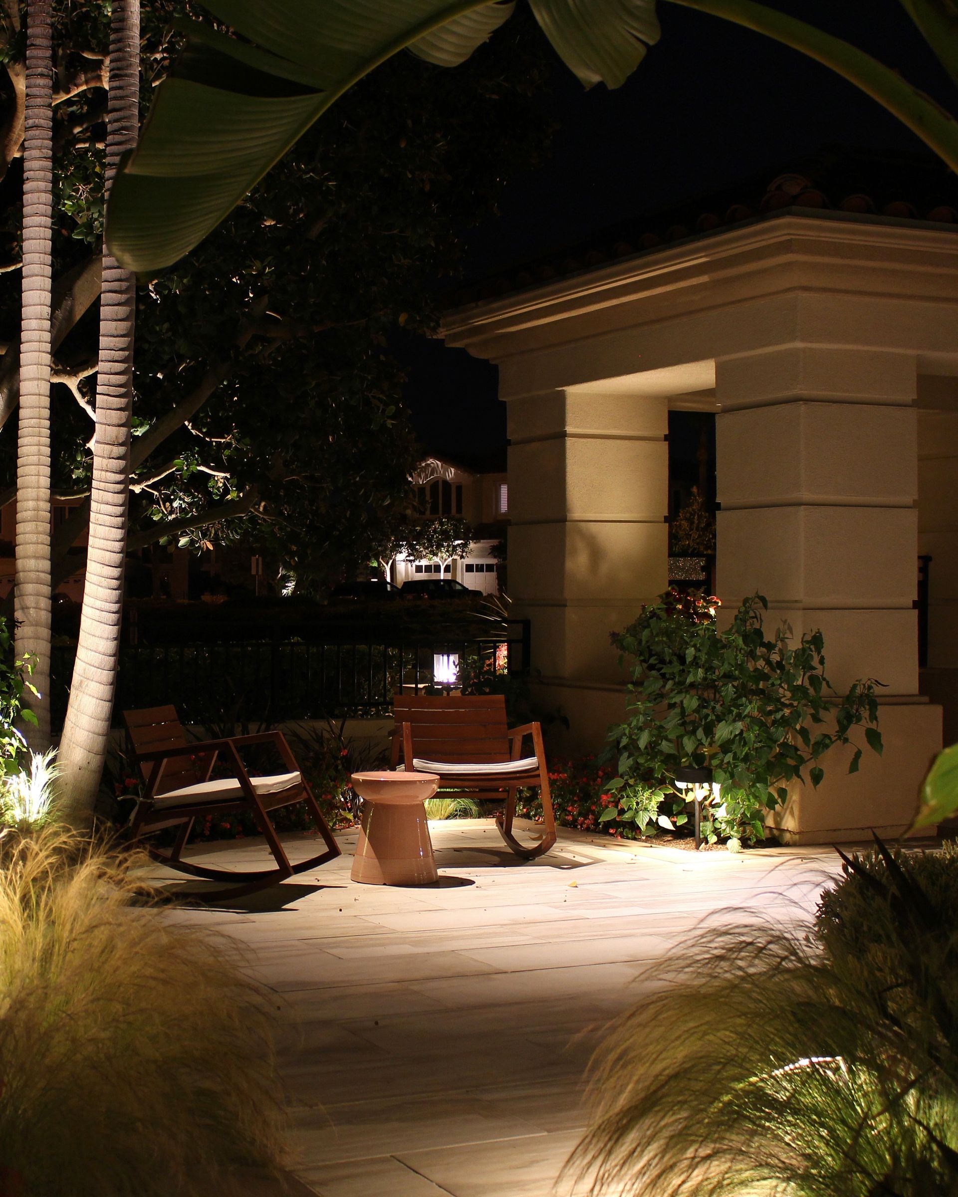 Lit garden walkway with a bench, potted plants, and a stone archway at night
