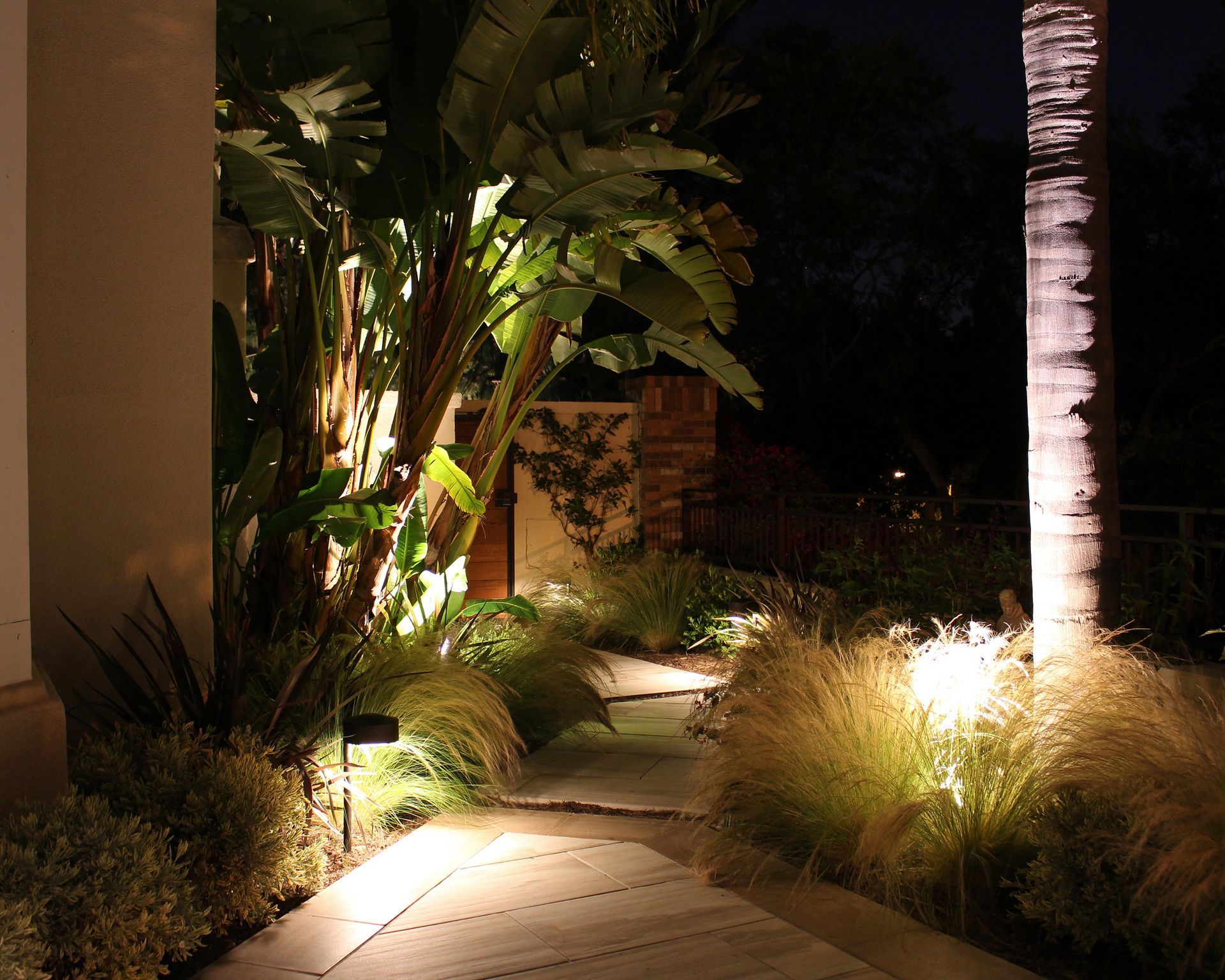Lit garden path with tropical plants, palm trees, and warm landscape lighting at night