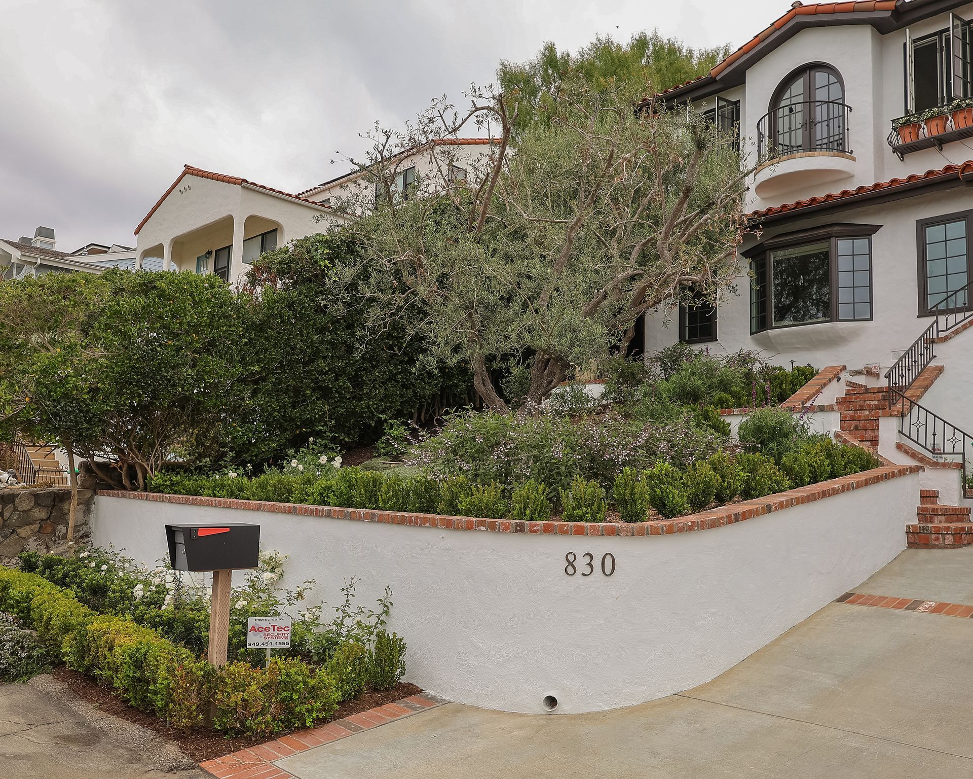 White stucco house with red tile roof, lush landscaping, and address number 830 at the curb.