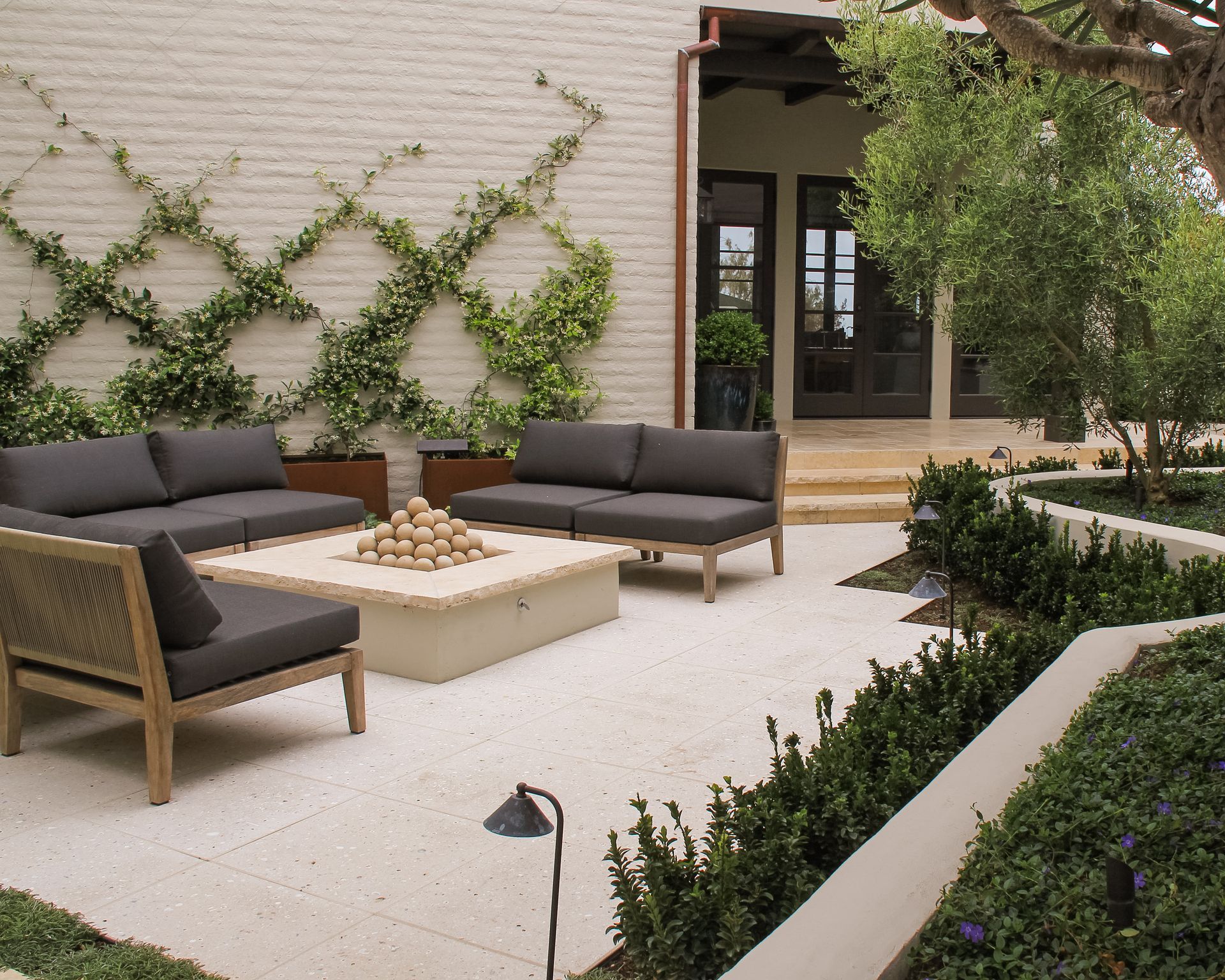 Modern patio with gray outdoor sofas, fire pit, ivy wall, and landscaped garden steps
