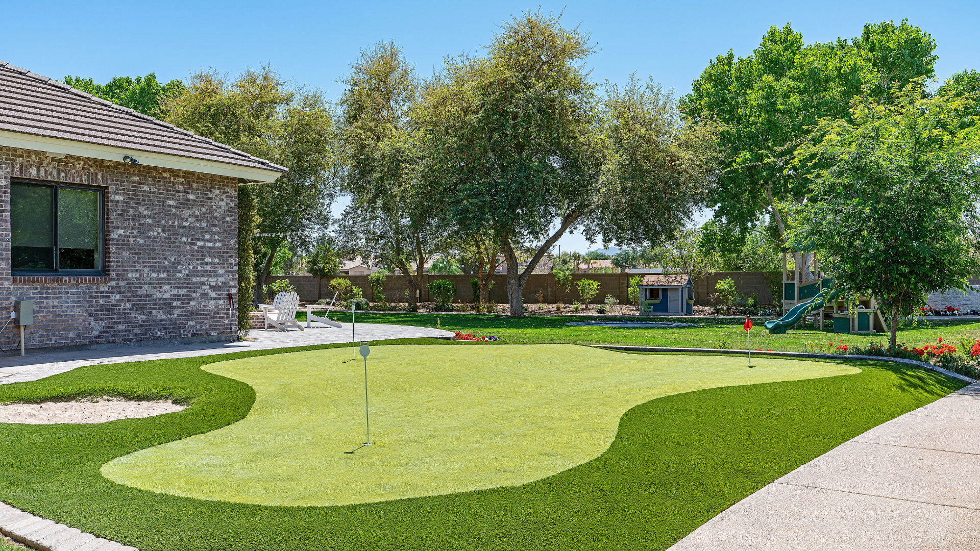 Landscaped backyard with green lawn, curving walkways, trees, and a stone house on the left