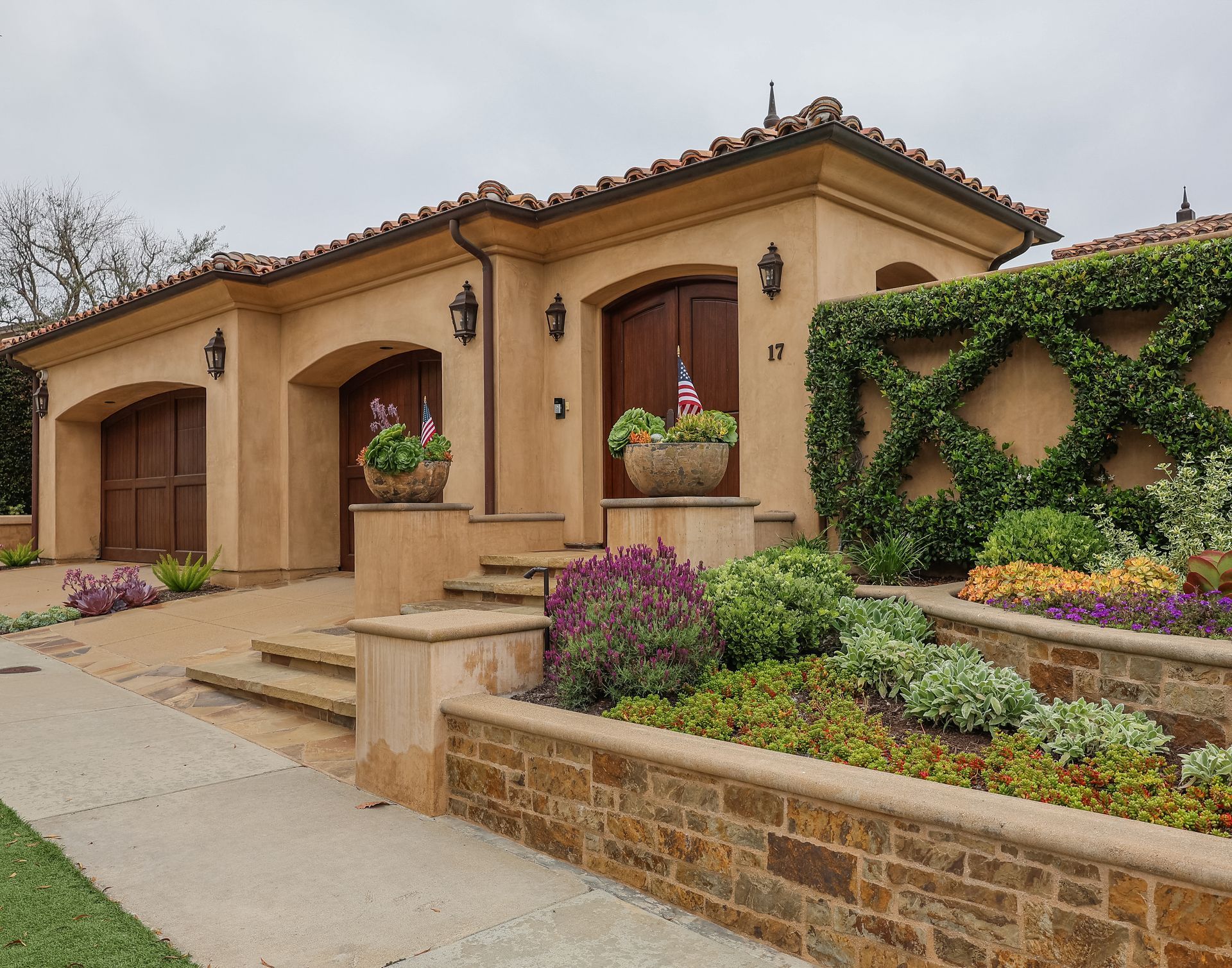 Stucco house with terracotta roof, arched porch, and landscaped front garden with flowers and ivy
