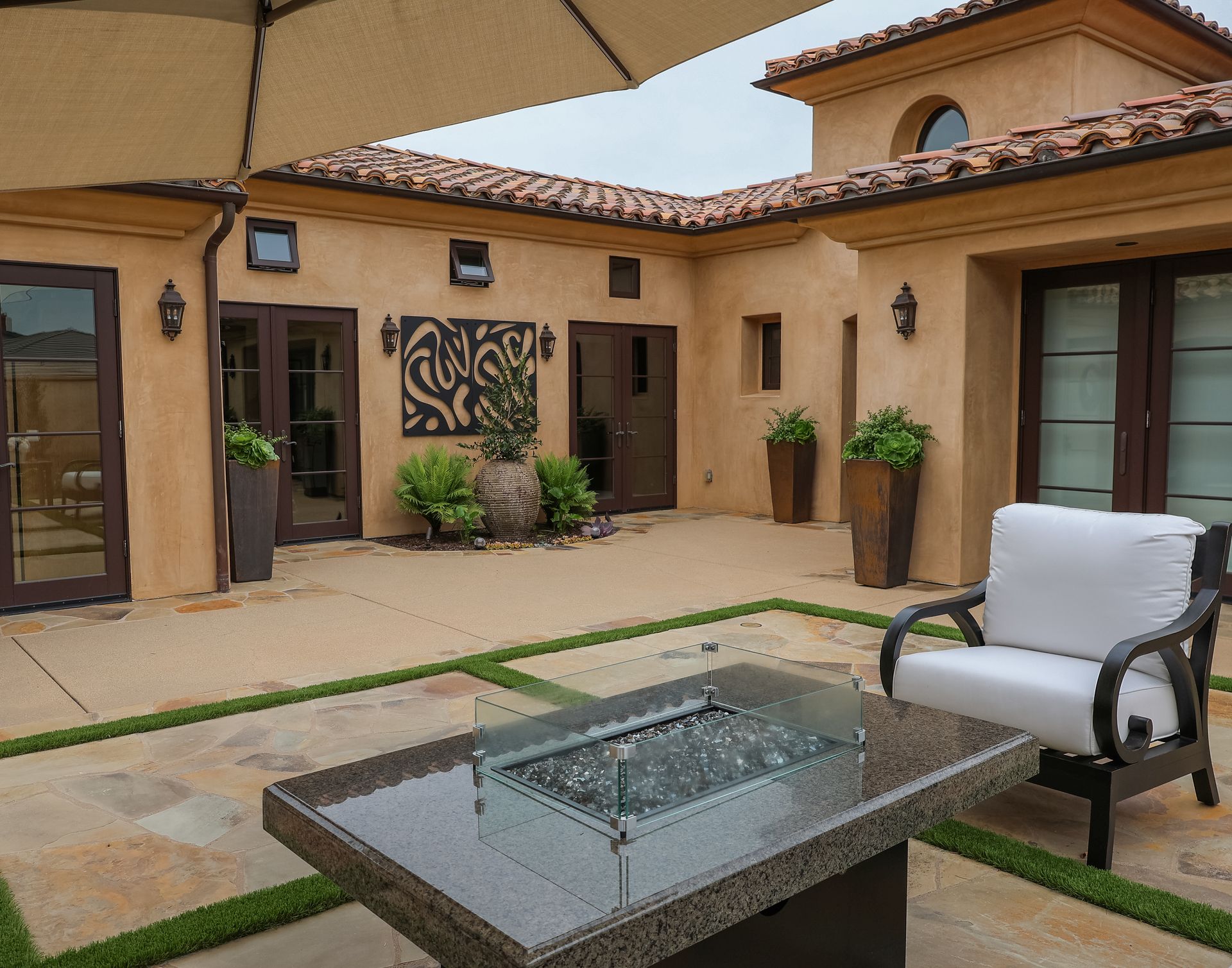 Courtyard patio with a glass fire table, lounge chair, and stucco walls under a canopy