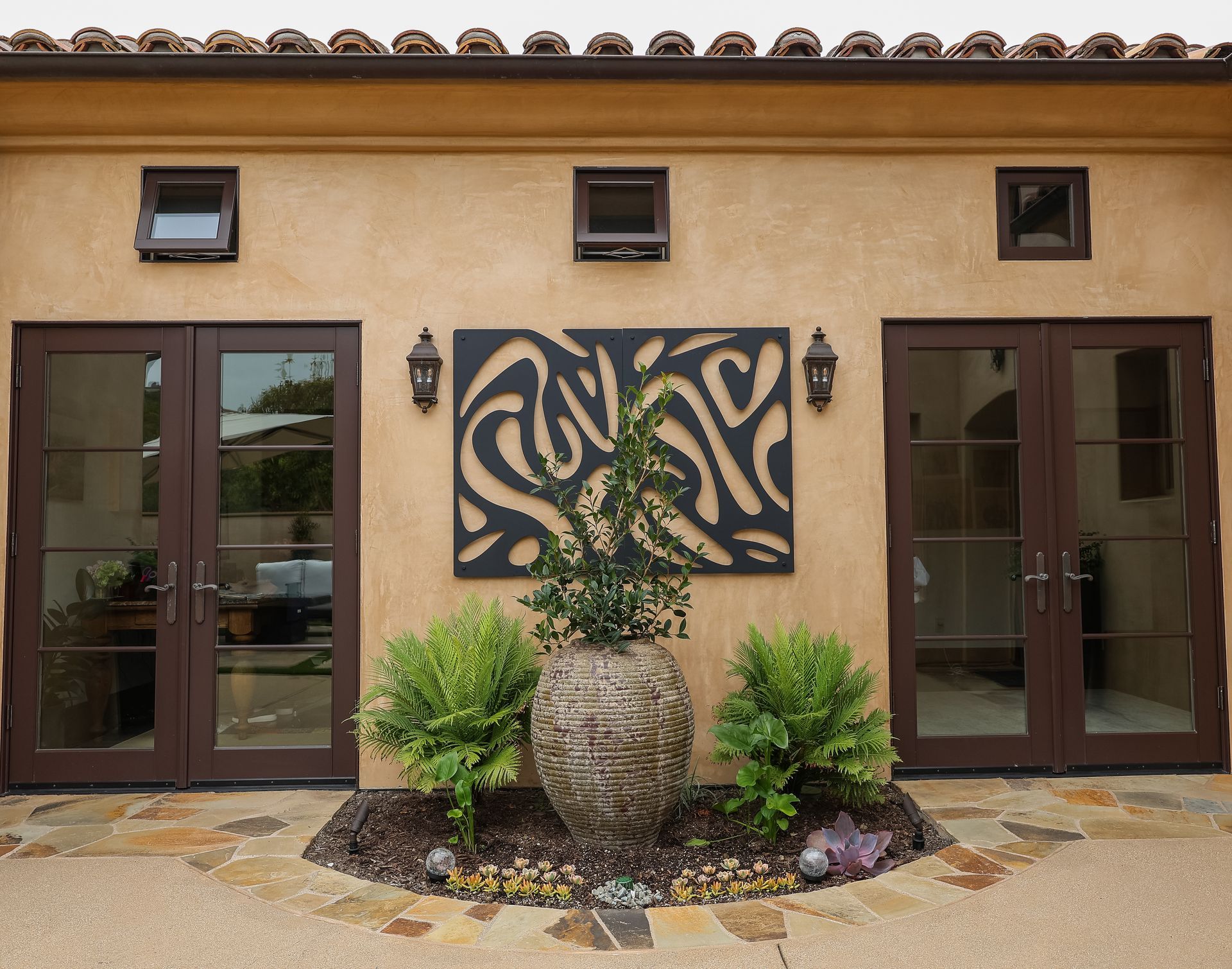 Front entrance of a building with double doors, decorative wall art, and a stone planter with greenery