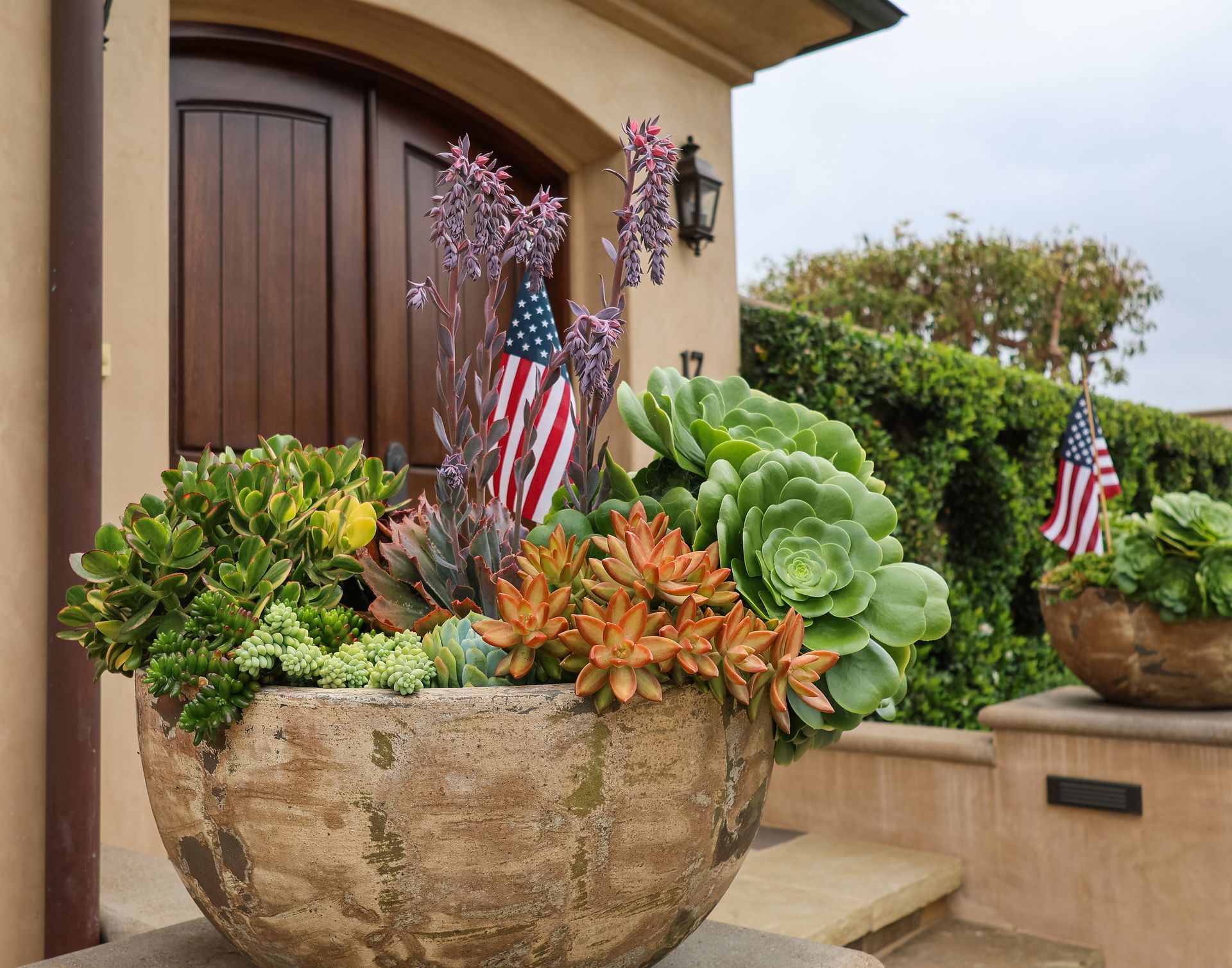 Large rustic planter with succulents and small American flags by a front doorway