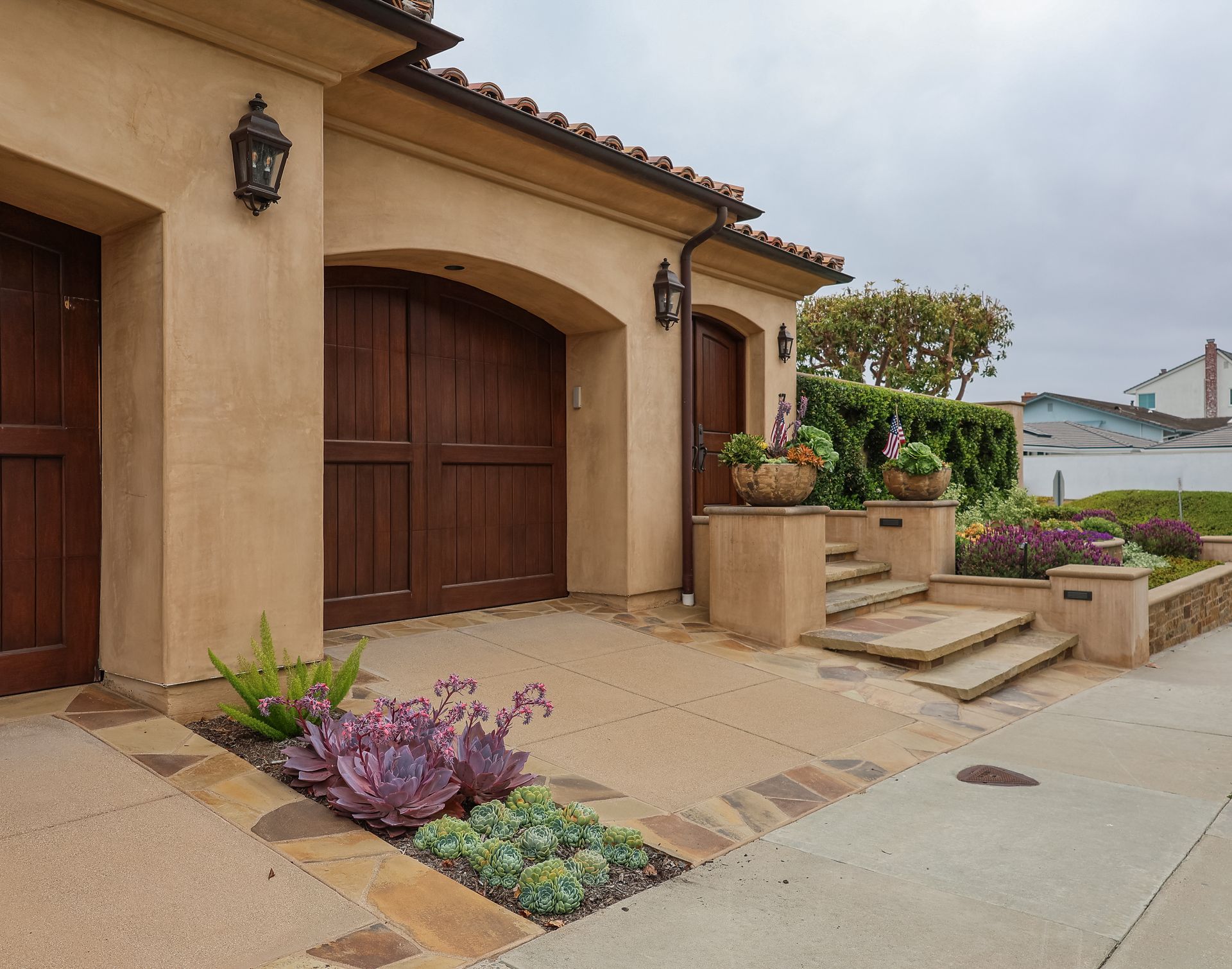 Spanish-style house entrance with wooden garage doors, stucco walls, and potted plants by the steps