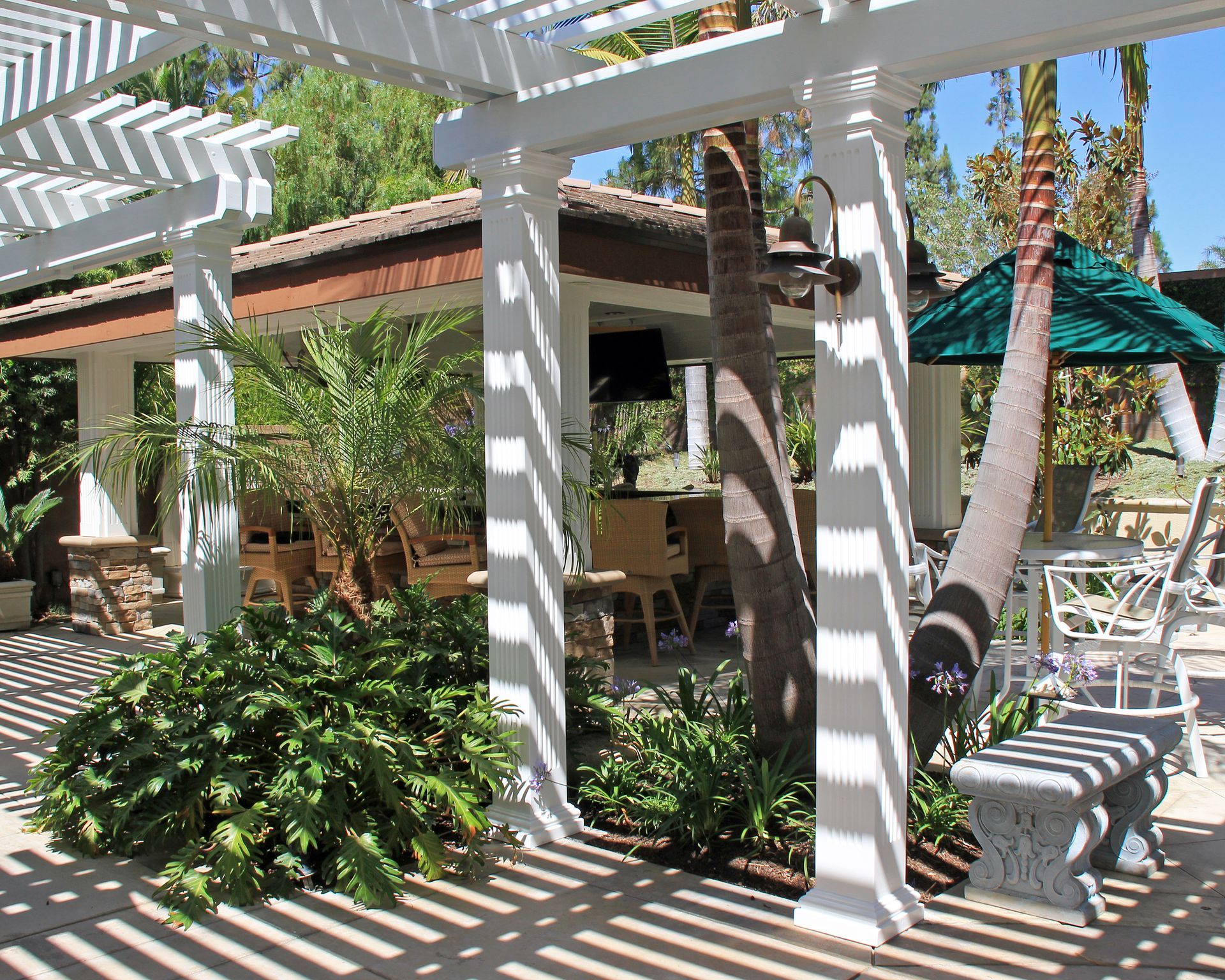 Shaded patio with white pergola, striped shadows, lounge chairs, and lush tropical plants