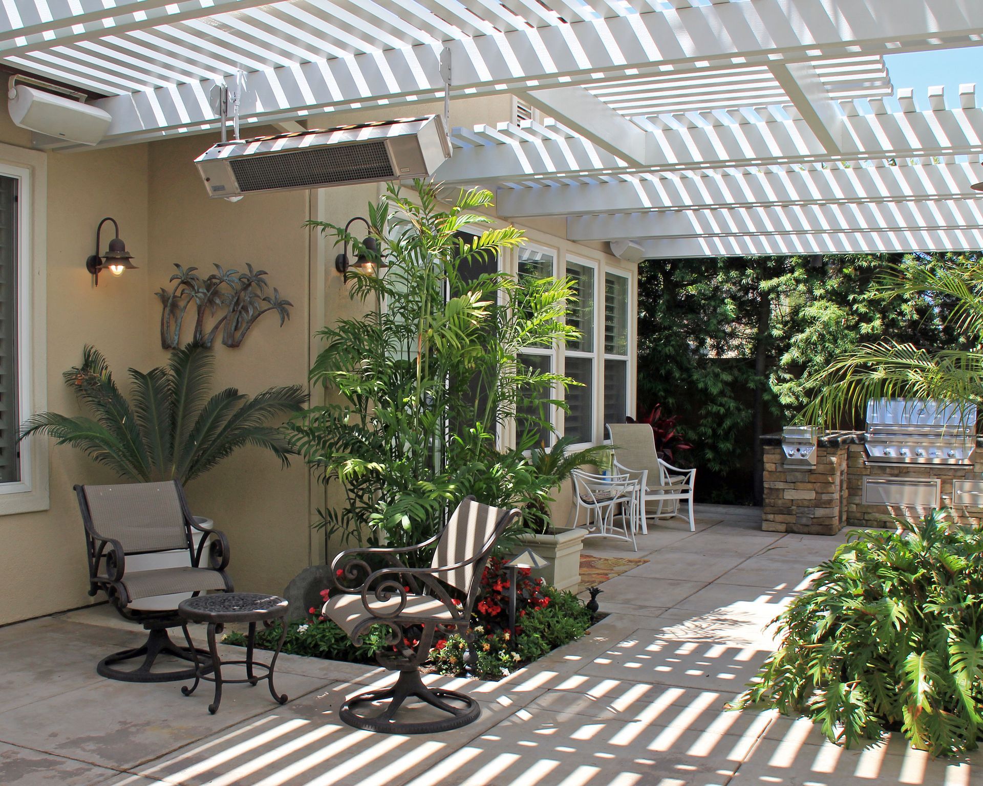 Shaded patio with lounge chairs, potted plants, and striped pergola shadows beside a garden walkway