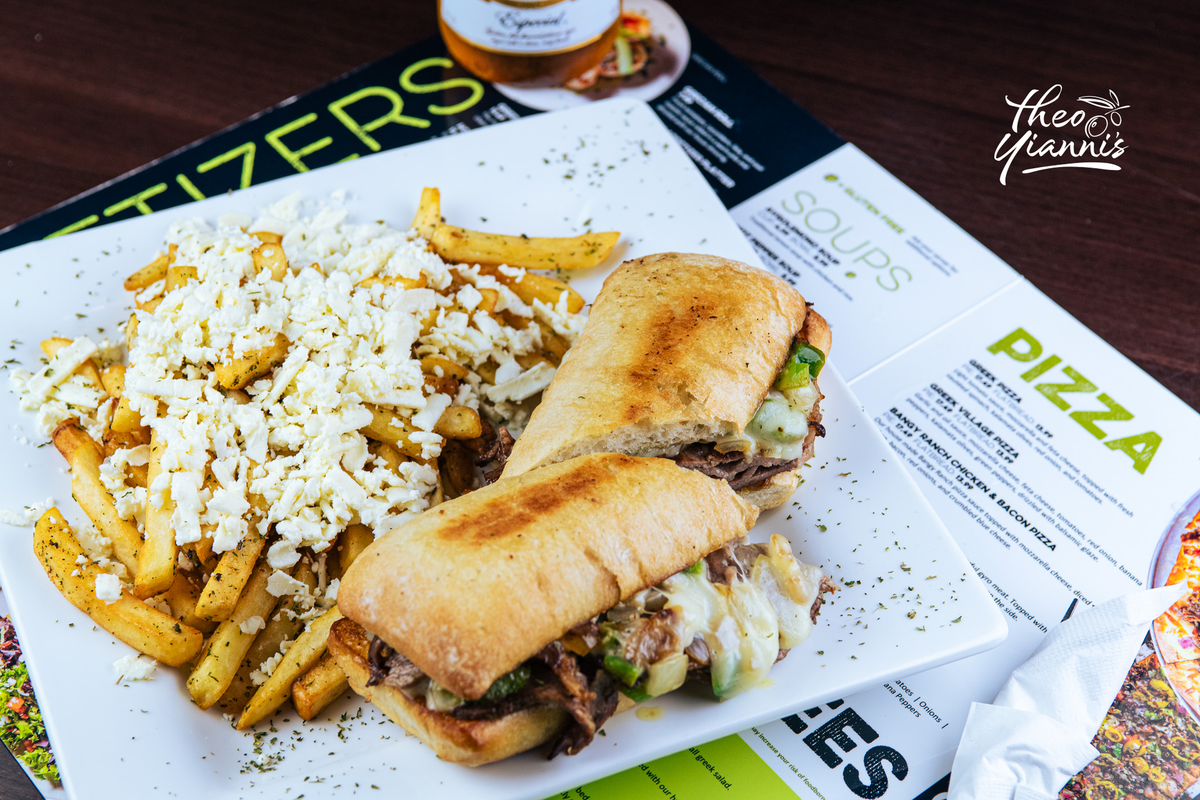 Grilled ciabatta sandwich with melted provolone beside Greek-style fries topped with feta