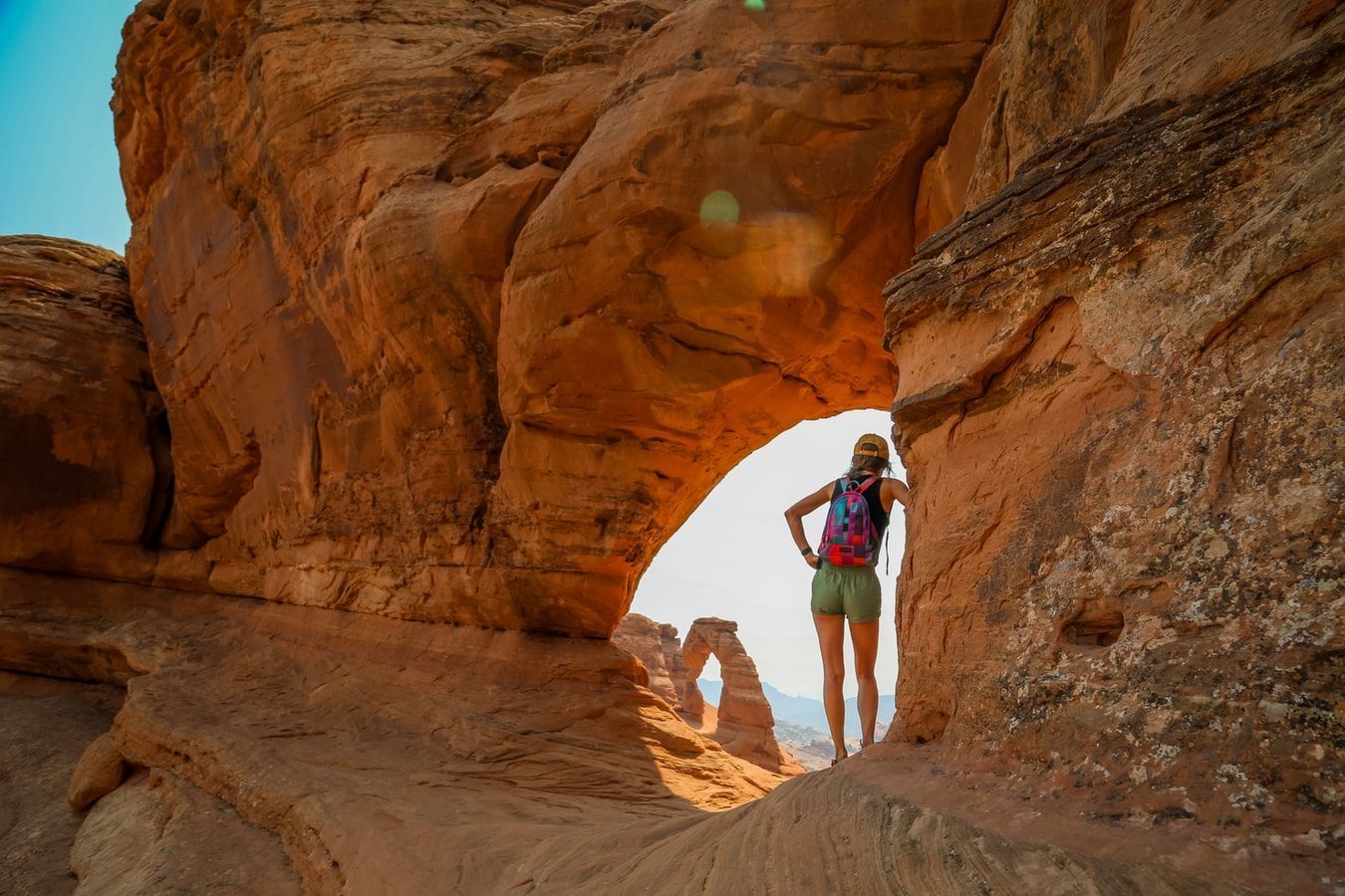 A woman is standing in a rock archway in the desert.