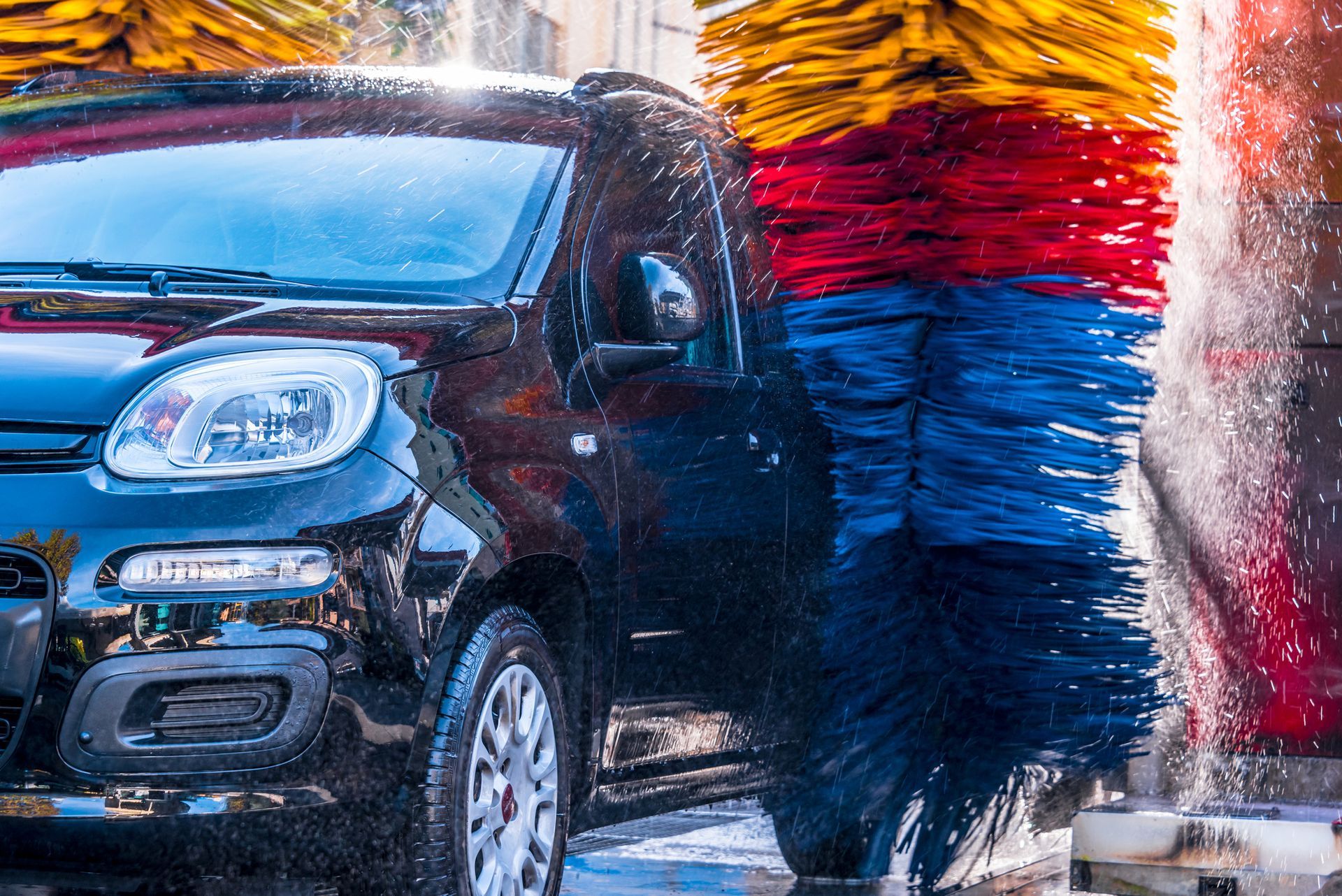 Camion nero in un autolavaggio automatico con spazzole rotanti colorate e getti d'acqua