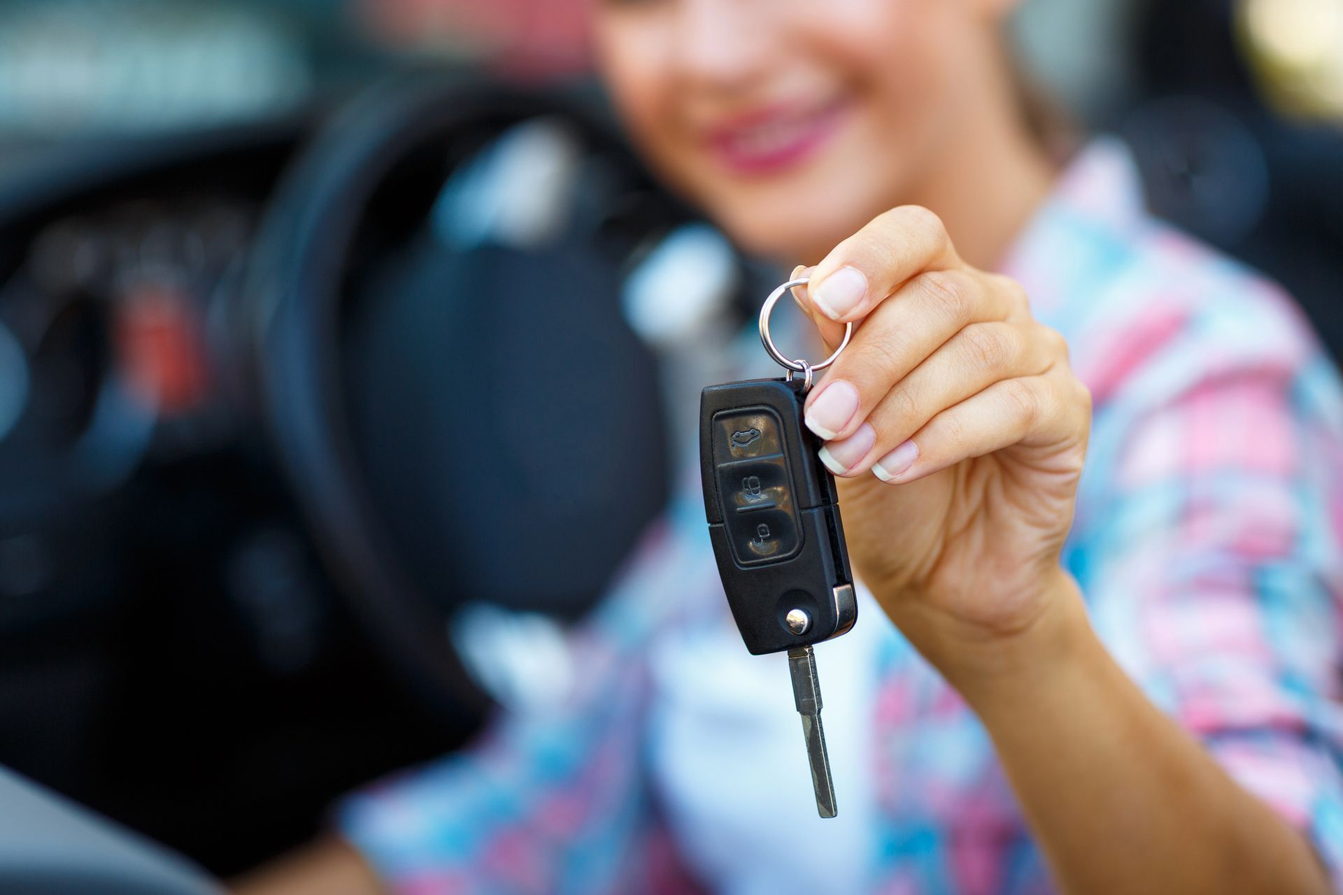 Mano che impugna il telecomando di un'auto davanti a una portiera aperta del veicolo.