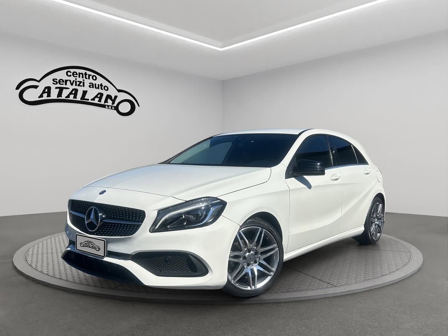 Berlina Mercedes-Benz bianca in uno showroom con il logo CATALANO sulla parete.