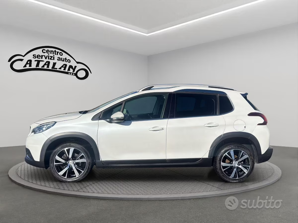 SUV bianco esposto in uno showroom, vista laterale, con insegna del marchio sullo sfondo.